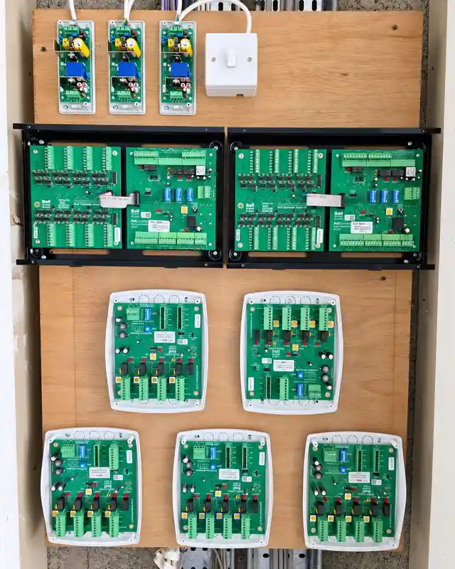 Plywood backboard in a cupboard with three power supplies, two banks of control boards and five distribution units, covers off.