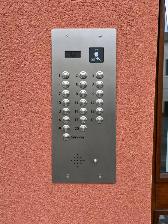 Stainless steel 20-button video door entry panel with camera and fob reader on pink rendered wall.