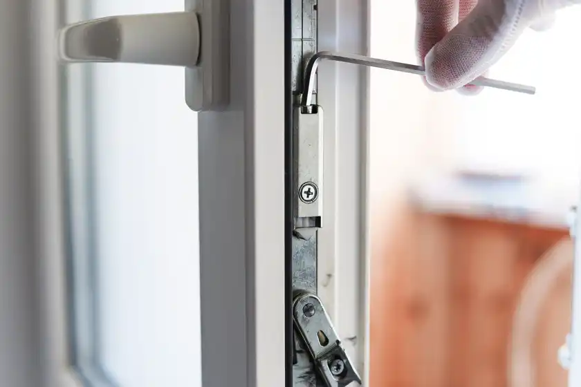 A gloved hand adjusting the locking gear on the edge of a white uPVC door with an Allen key.