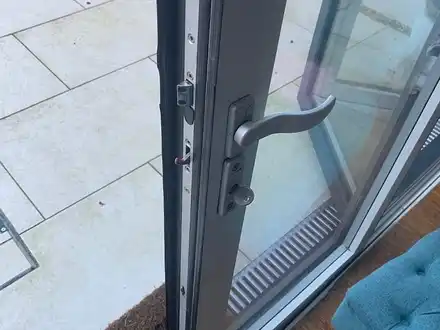 The edge of an open grey patio door, showing its multipoint lock, handle and key.