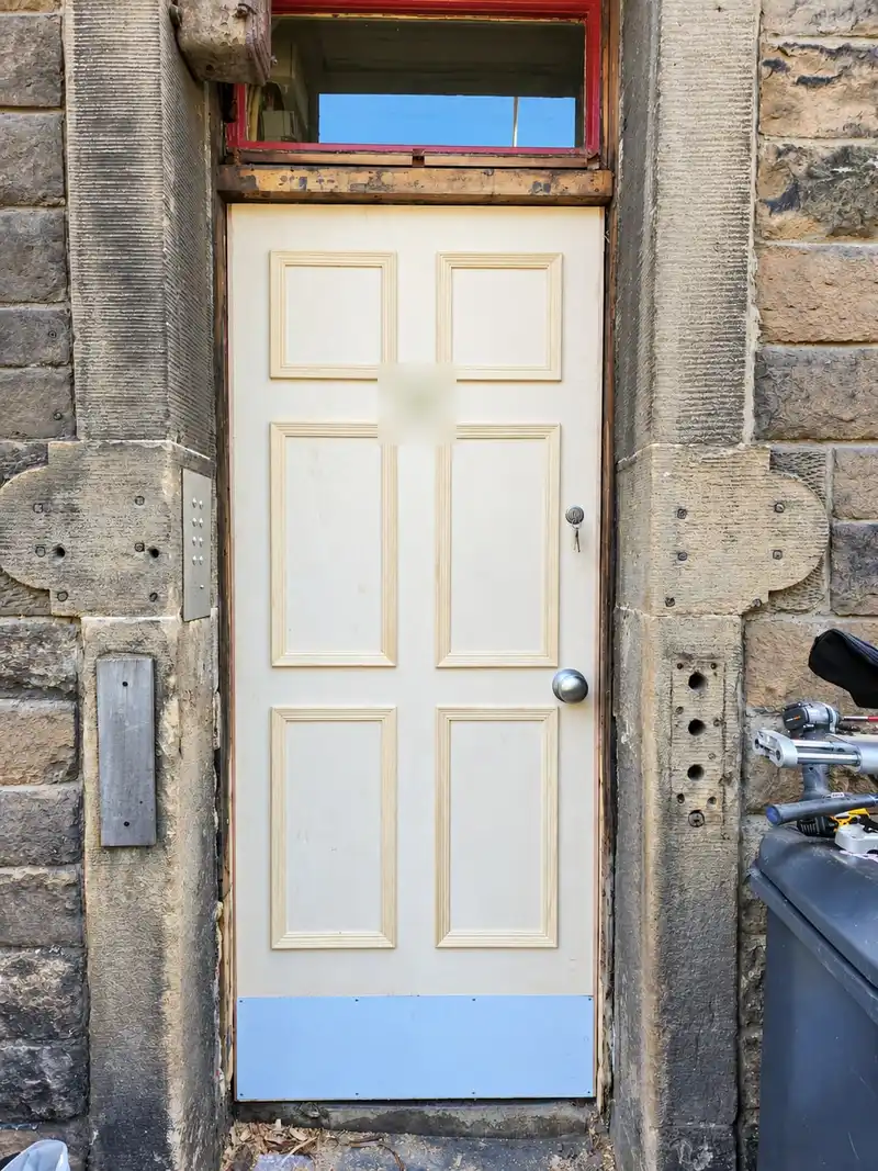 New unpainted six-panel timber door with a kick plate, fitted in the same stone doorway.