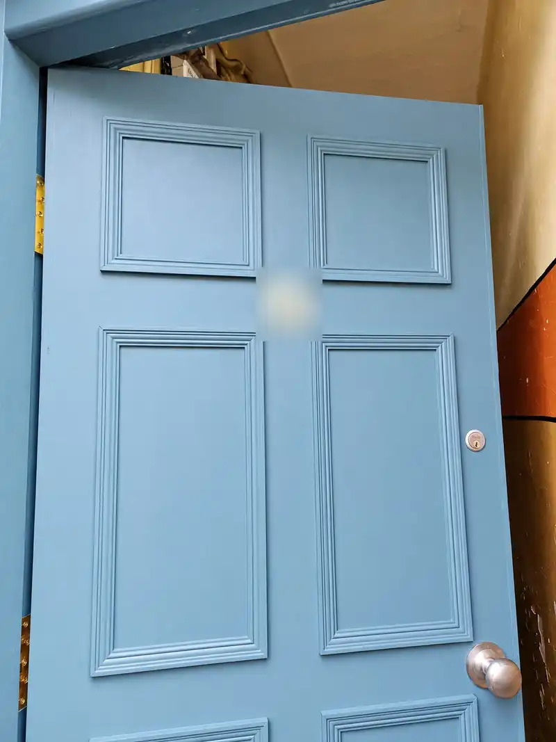 The painted teal-blue six-panel door seen from an angle, standing open.