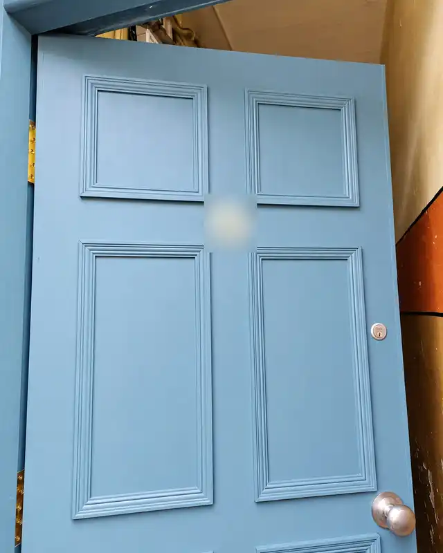The painted teal-blue six-panel door seen from an angle, standing open.