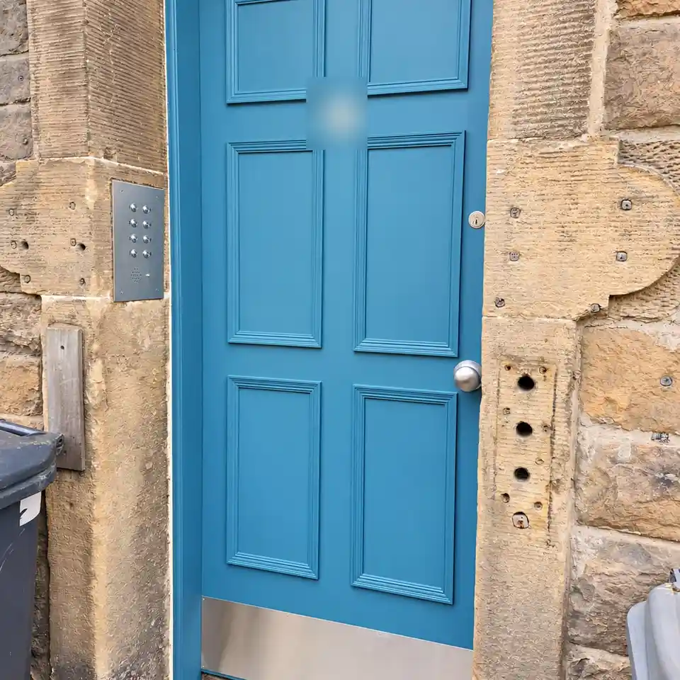 The new six-panel door painted teal-blue, with a steel kick plate and an entry panel on the wall to the left.