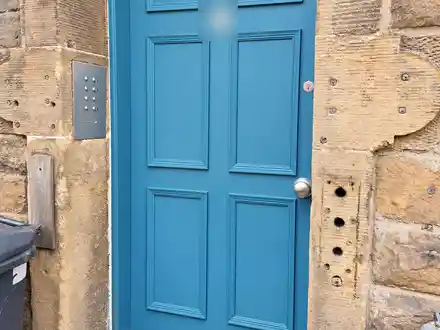 The new six-panel door painted teal-blue, with a steel kick plate and an entry panel on the wall to the left.