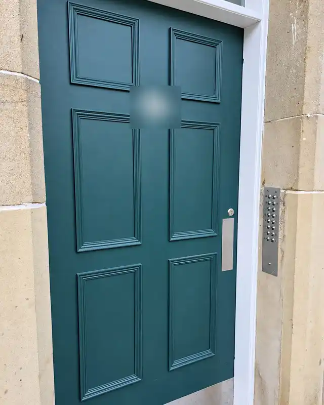 Close view of the new dark green six-panel stair door with a letter plate and a stainless door entry panel on the stone beside it.