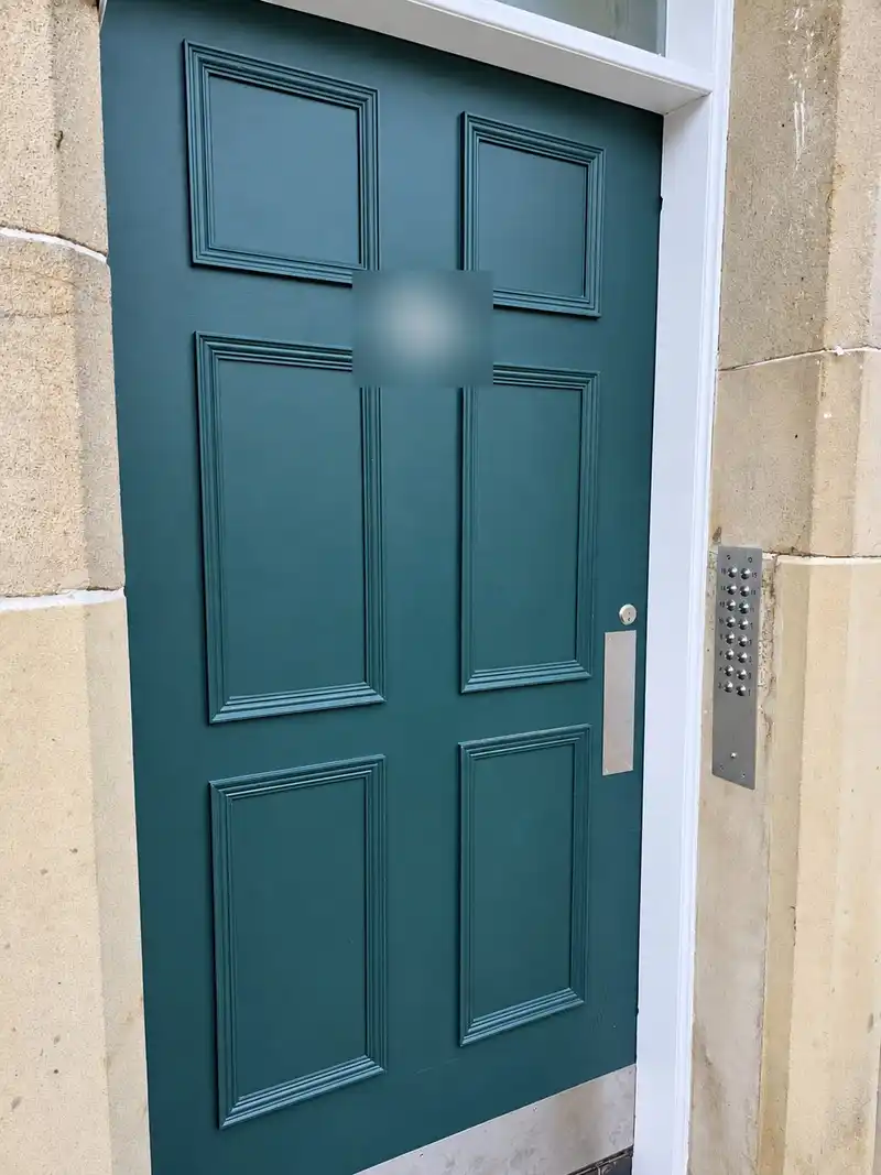 Close view of the new dark green six-panel stair door with a letter plate and a stainless door entry panel on the stone beside it.