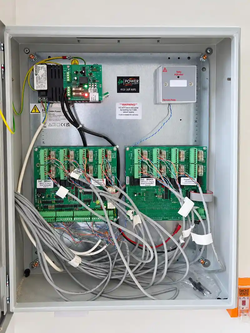 Open grey enclosure showing door entry control boards, a power supply and neatly labelled cables.