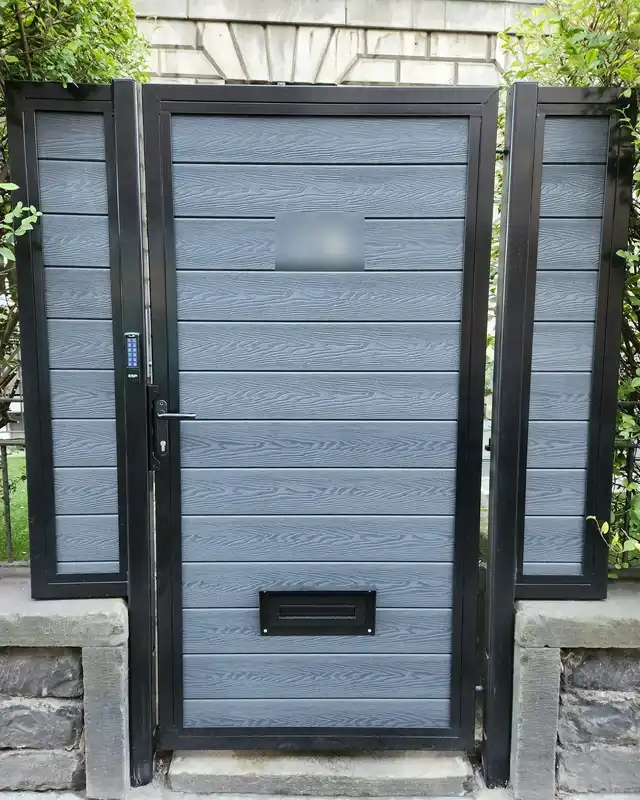 Grey composite garden gate in a black frame with a letter plate, a lever handle and a keypad on the frame.