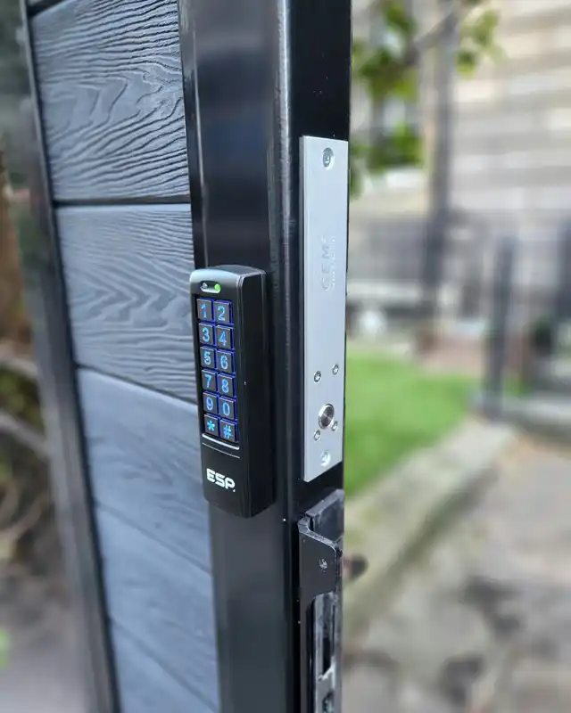 Keypad on a black gate post beside the magnetic lock plate that holds the gate shut.