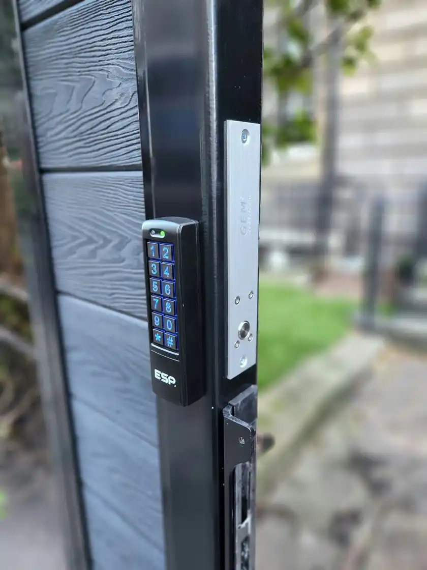 Keypad on a black gate post beside the magnetic lock plate that holds the gate shut.