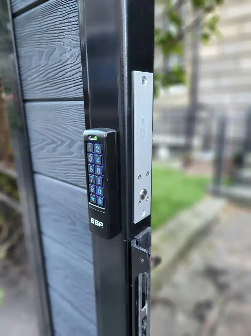 Keypad on a black gate post beside the magnetic lock plate that holds the gate shut.