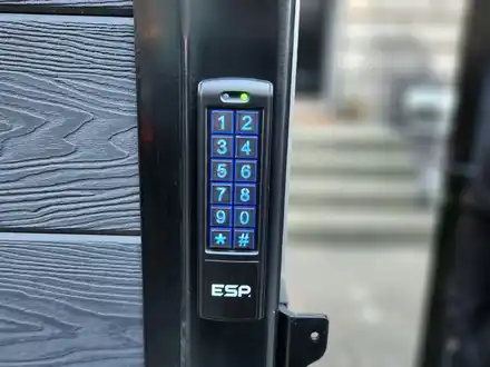 Illuminated blue keypad on the black frame of a grey garden gate.