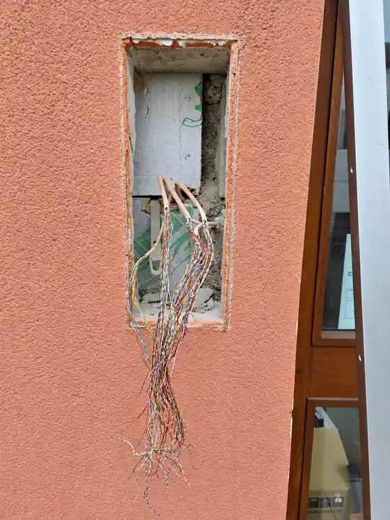 Rectangular hole in a pink rendered wall with loose cables where an old door entry panel has been taken out.