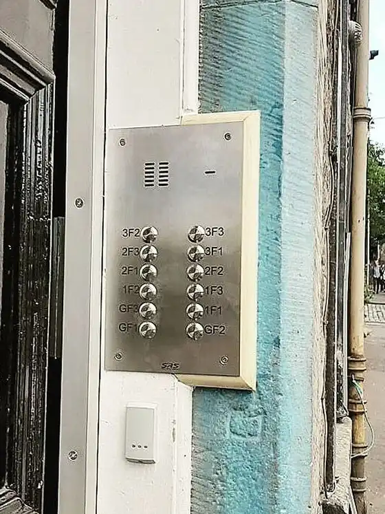 New stainless steel door entry panel with buttons labelled by flat position, beside a tenement door.