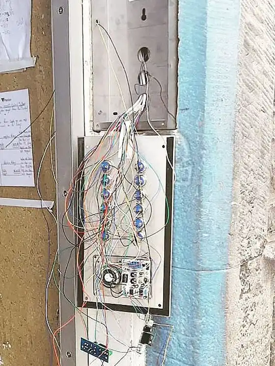 Old door entry panel opened on a weathered wall with the wiring exposed.