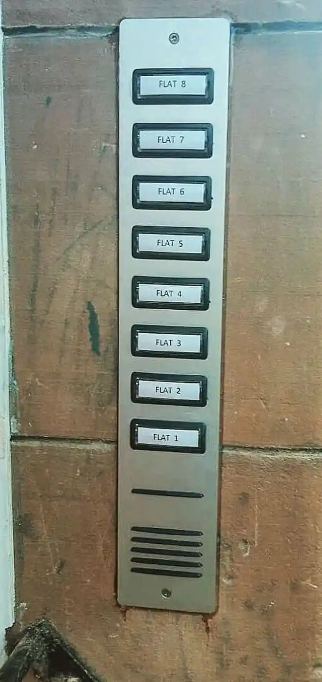 The same stone wall with a finished eight-button door entry panel labelled Flat 1 to Flat 8.