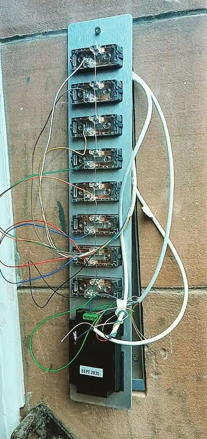 Door entry panel opened on a stone wall, with the button switches and loose wiring visible.