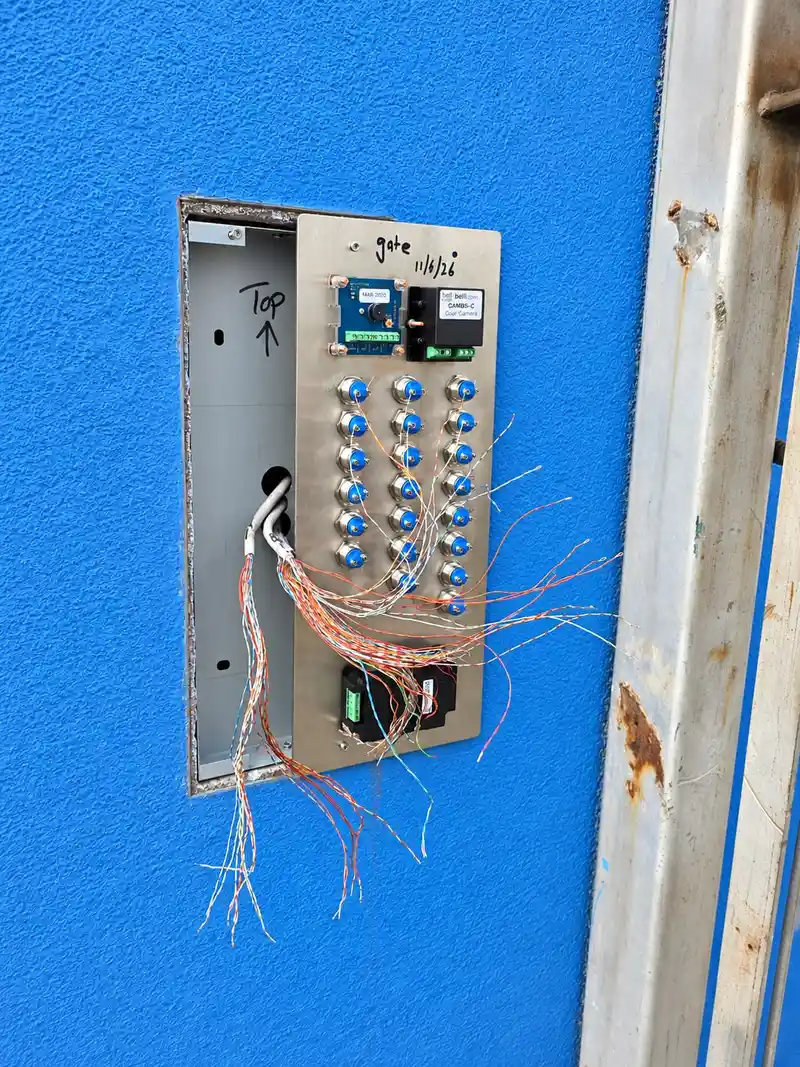 Door entry panel pulled forward from a blue wall during installation, with its cable cores being connected to the button module.