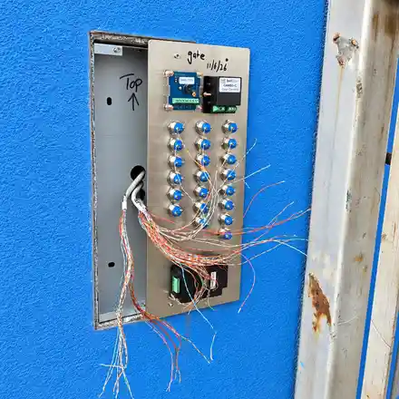 Door entry panel pulled forward from a blue wall during installation, with its cable cores being connected to the button module.