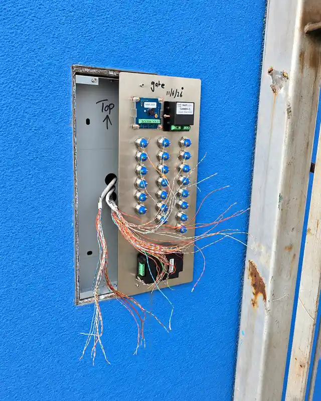 Door entry panel pulled forward from a blue wall during installation, with its cable cores being connected to the button module.