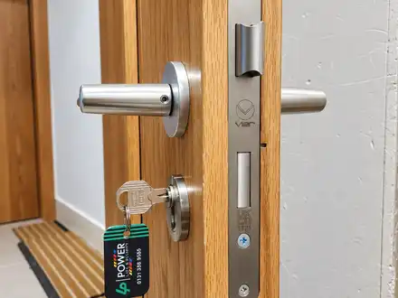 Satin steel lever handle and mortice sashlock on an oak-veneer door, with a corridor behind.