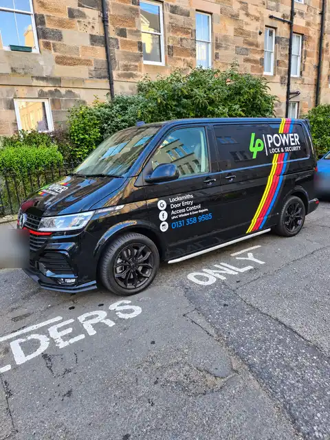 Front three-quarter view of the black Power Lock & Security van parked beside a sandstone tenement.