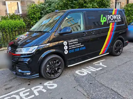 Front three-quarter view of the black Power Lock & Security van parked beside a sandstone tenement.