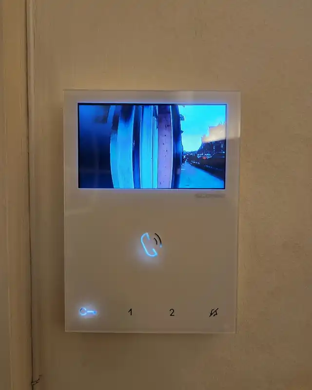 White video entry monitor on a flat wall, its screen showing the view from the street door camera.