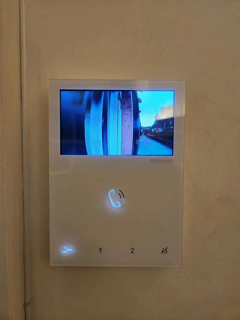 White video entry monitor on a flat wall, its screen showing the view from the street door camera.