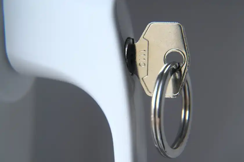 A white locking window handle with its key in the lock.