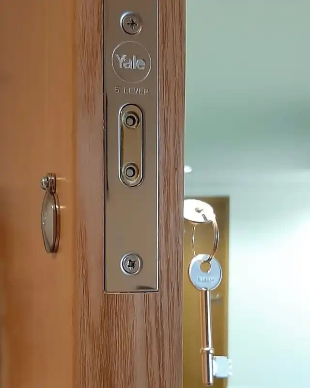 Forend of a Yale five-lever mortice lock on an oak-effect door, with a key hanging from the lock.