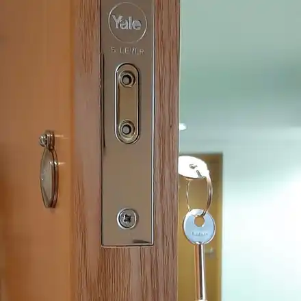 Forend of a Yale five-lever mortice lock on an oak-effect door, with a key hanging from the lock.