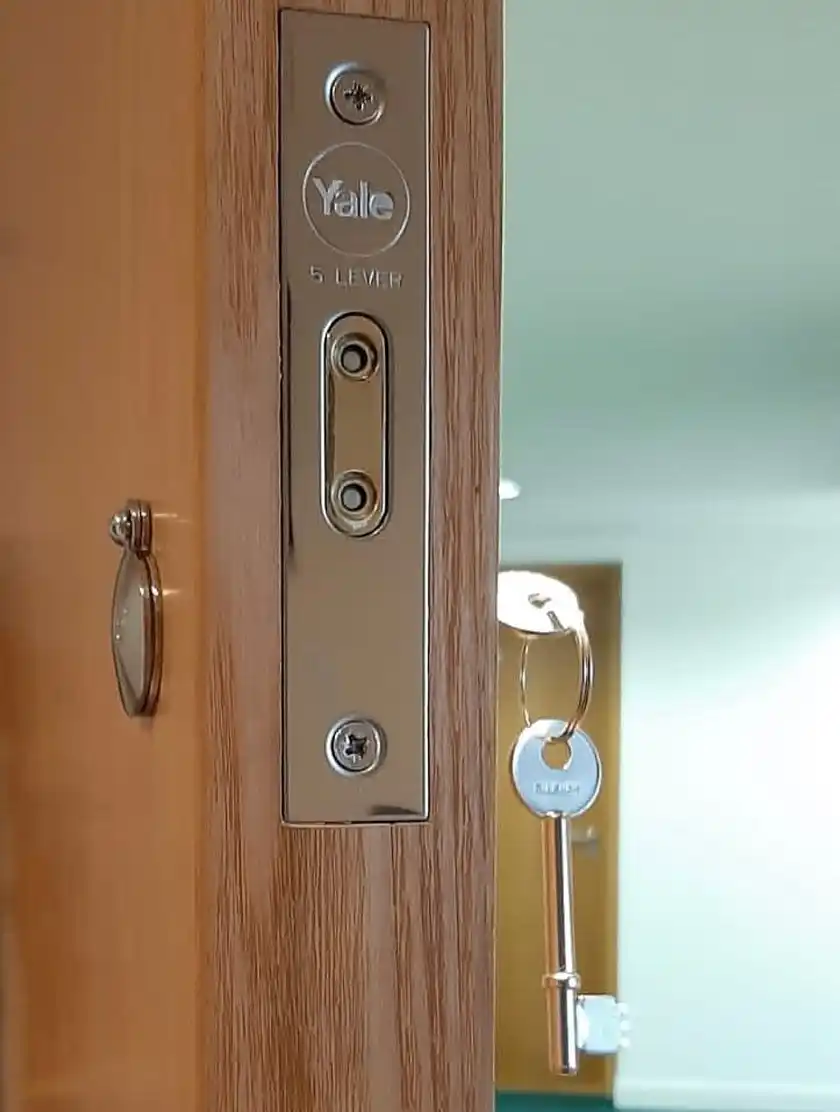 Forend of a Yale five-lever mortice lock on an oak-effect door, with a key hanging from the lock.